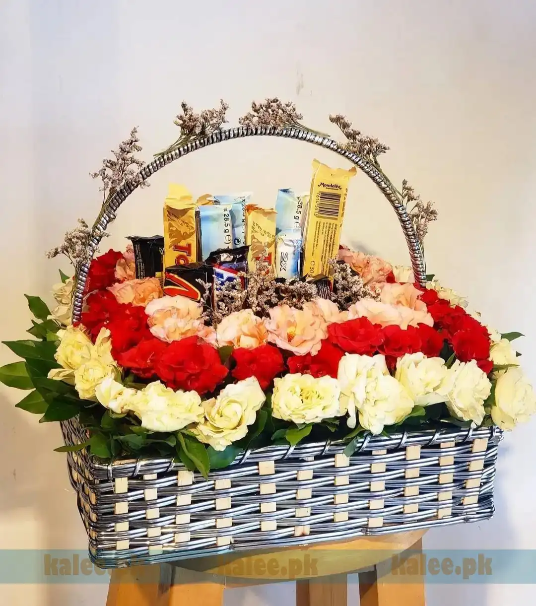 A luxurious Chocolates Basket featuring creamy white, red, and pink flowers paired with premium chocolates, including 3 Toblerone, 2 Bounty, 2 Mars, and 1 Snickers.