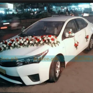 A car adorned with a decorative arrangement of red and pink roses and white glades.