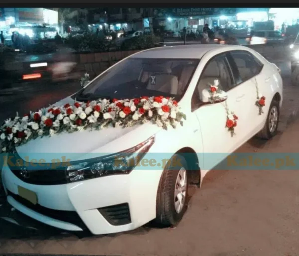 A car adorned with a decorative arrangement of red and pink roses and white glades.