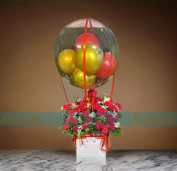 A floral arrangement in a box with red roses, baby's breath, and a balloon.