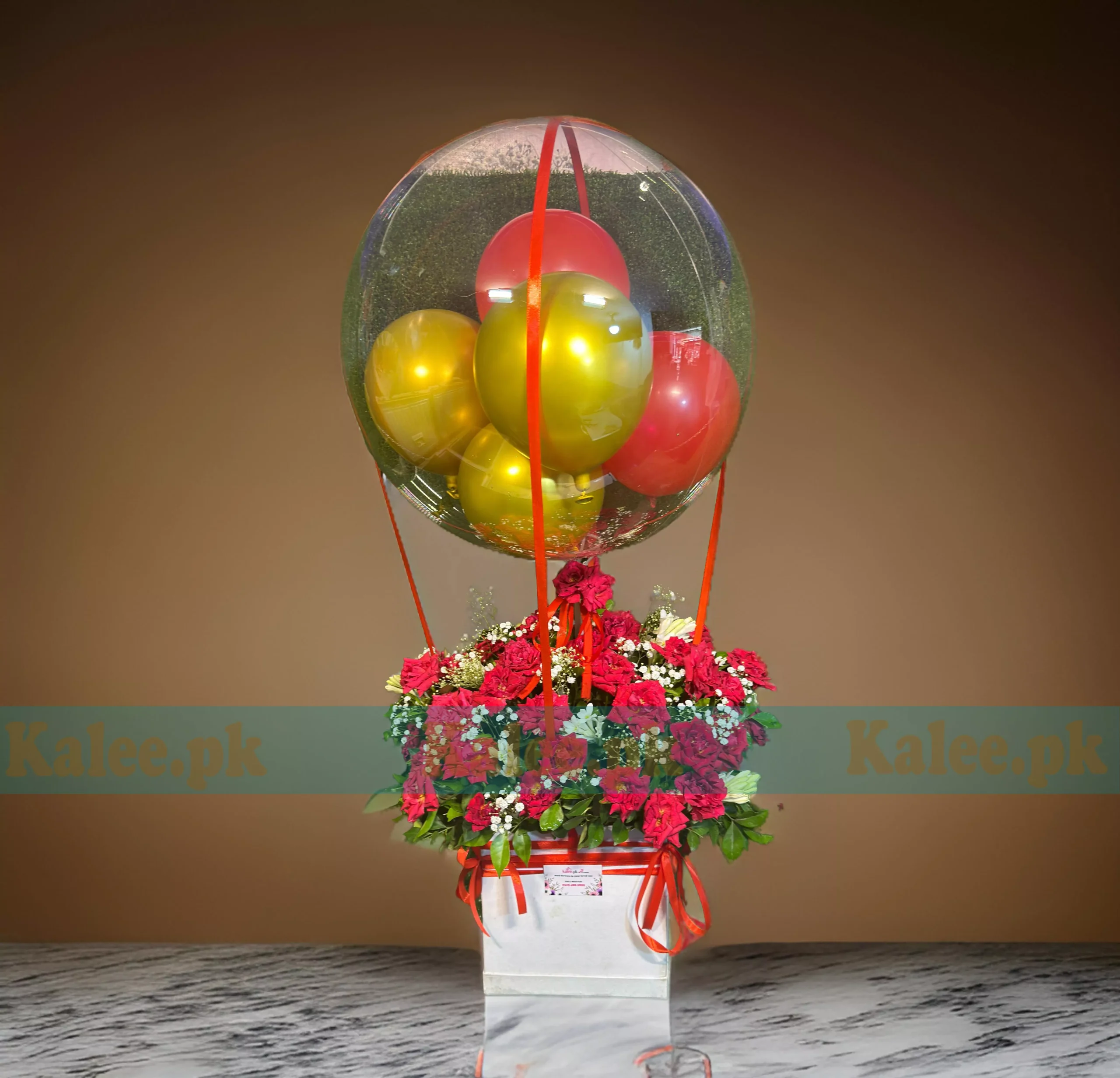 A floral arrangement in a box with red roses, baby's breath, and a balloon.