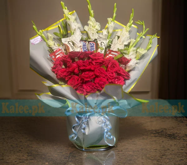 A bouquet featuring chocolates, white glades, and red roses.